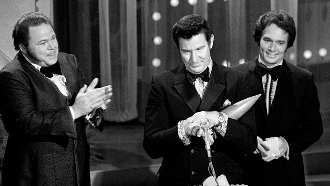 Freddie Hart, center, speaks to the audience after winning the Song of the Year for "Easy Lovin" at the CMA Awards show during the nationally televised ceremonies at the Grand Ole Opry House on Oct. 10, 1971. Looking on are presenters Roy Clark, left, and Merle Haggard.